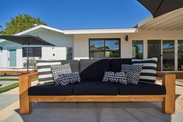 Teak outdoor sofa with striped and graphic cushions against white stucco