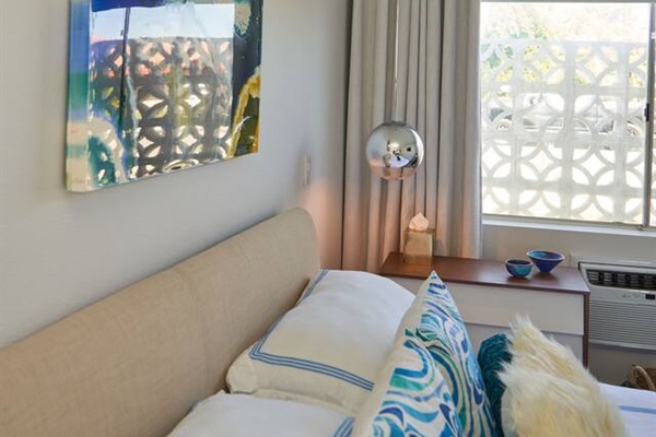 Guest bed with oatmeal linen headboard, chrome globe sconce and abstract canvas