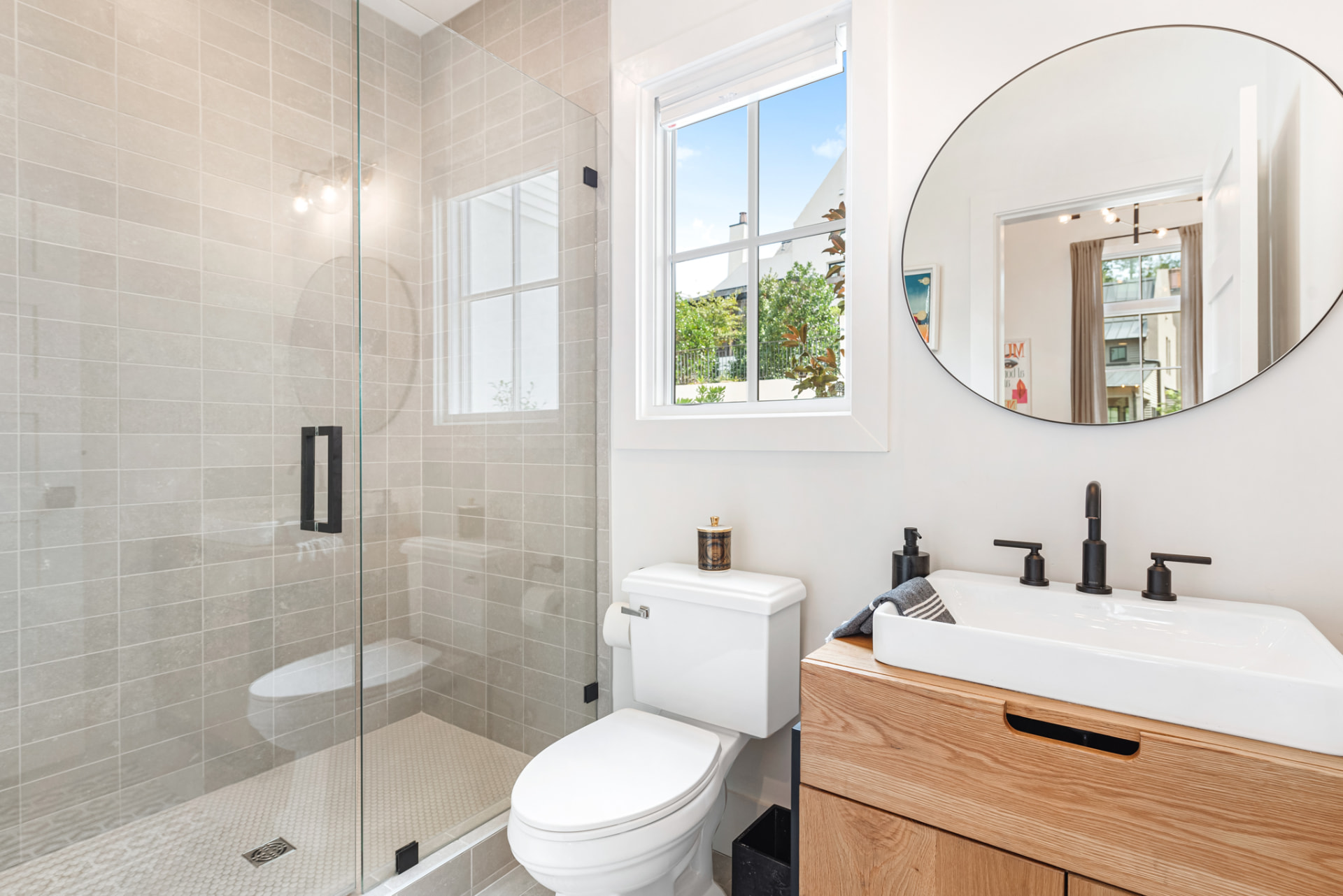 Guest bath with stone-grey stack tile shower, oak vanity and round black mirror