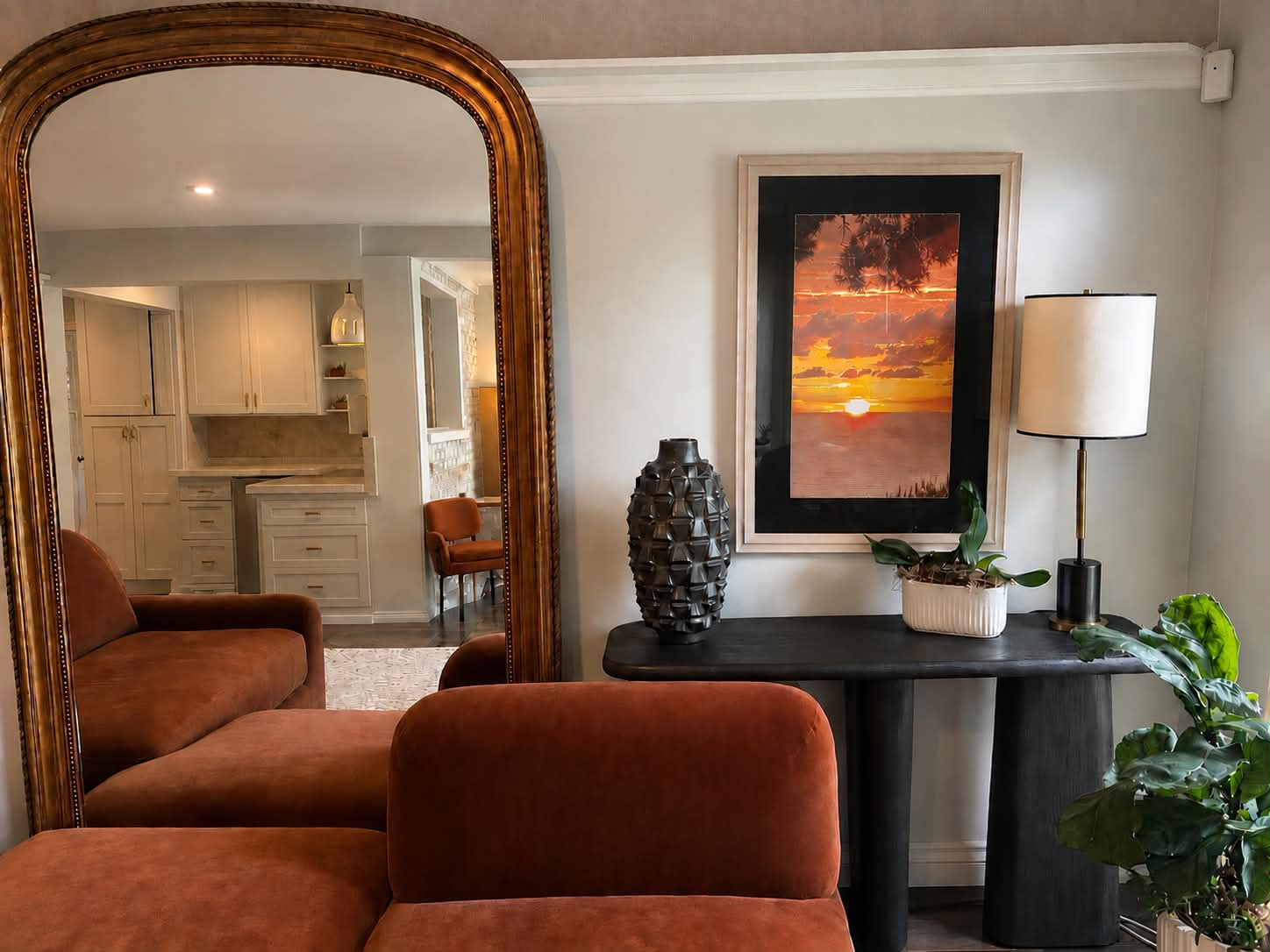 Sitting room with rust velvet seating, gilt arched mirror and blackened oval console