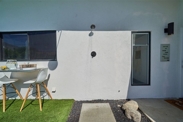 Outdoor shower on a white stucco wall beside a small dining setting
