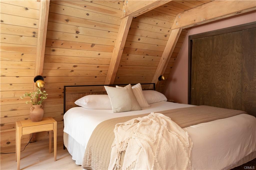 Bedroom with blush plaster wall, oak nightstand and brass globe sconces