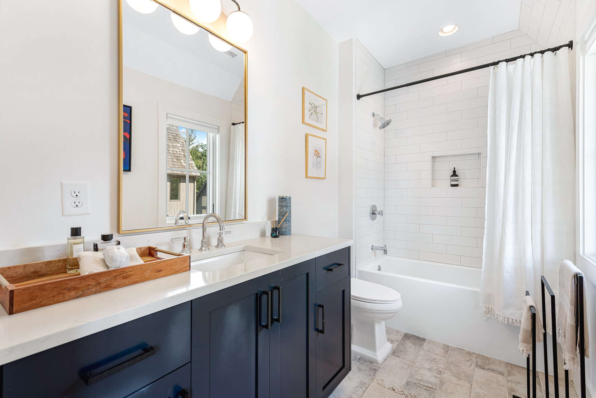 Guest bath with navy vanity, gilt mirror and white subway-tiled tub