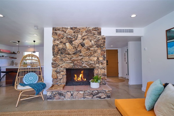 Stone fireplace alight with rattan hanging chair and orange daybed