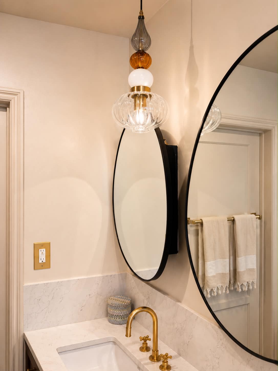 Blush plaster bath with black oval mirror and blown-glass pendant