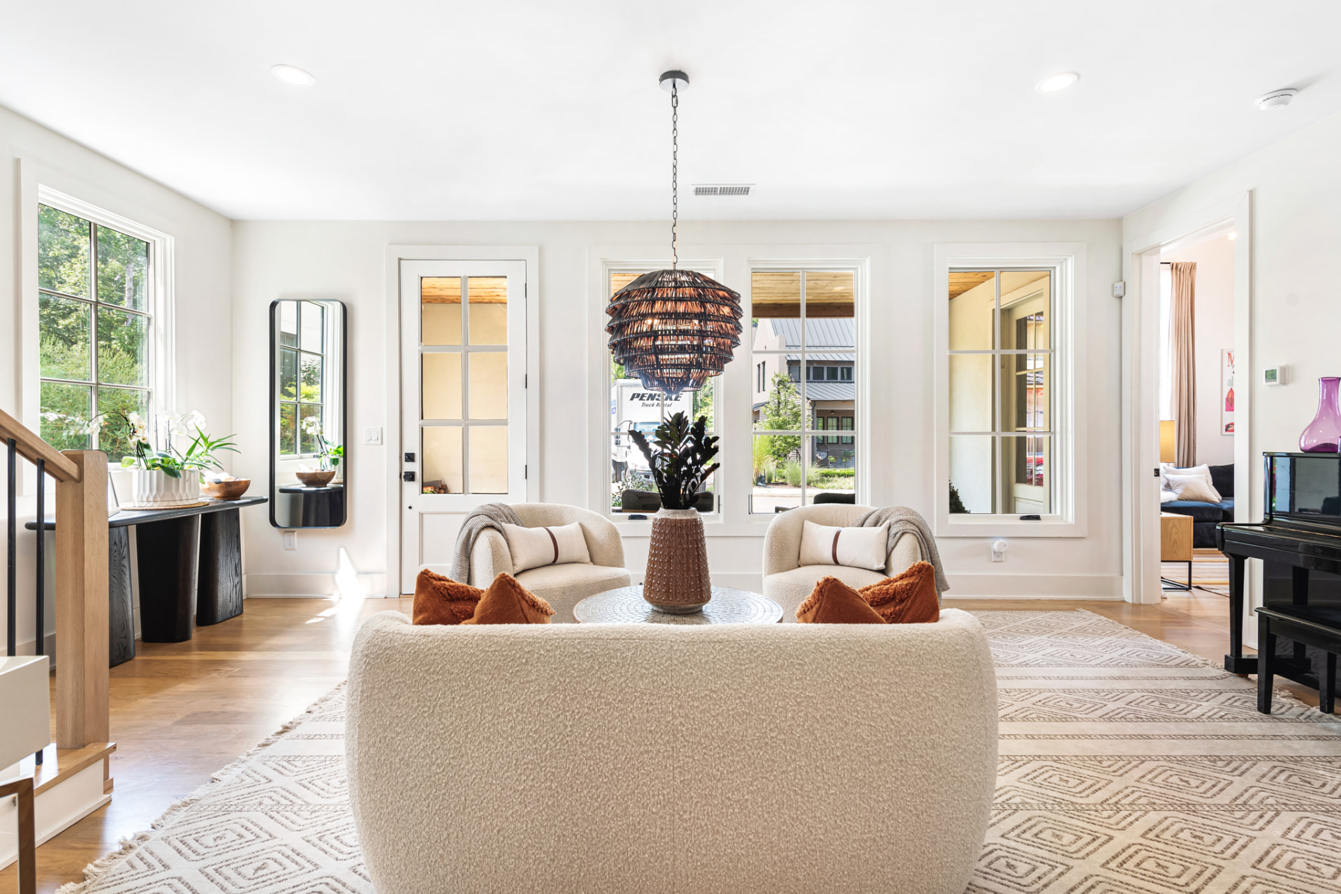 Sitting room facing the window wall with paired bouclé chairs and woven pendant