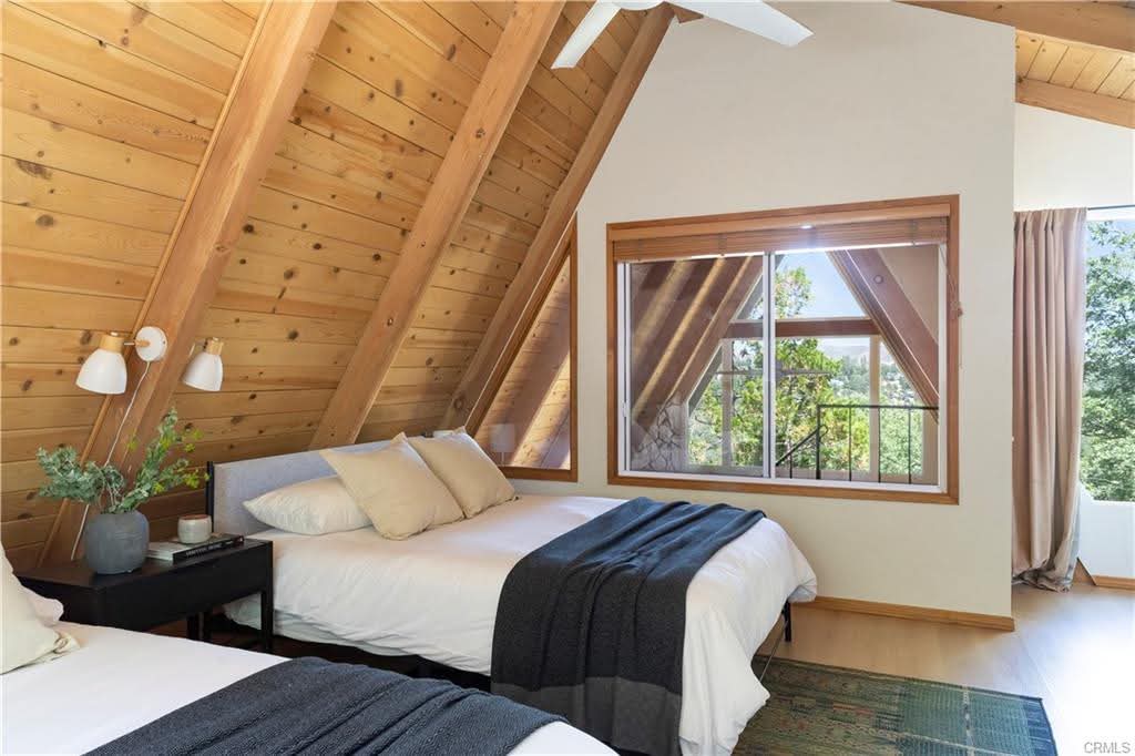 Twin bedroom under a pine A-frame ceiling with white sconces and charcoal throws