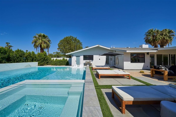 Infinity-edge pool, lawn strips and teak chaises along the terrace