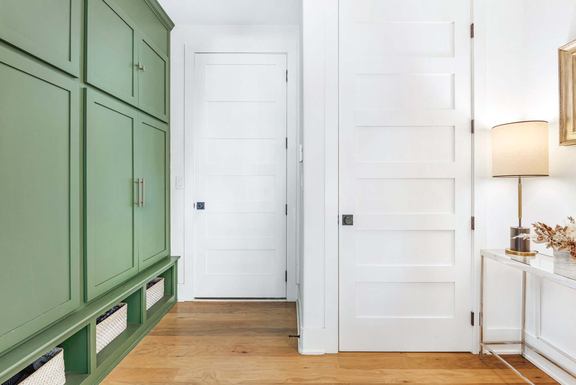 Mudroom with sage-green panelled lockers, woven baskets and white panel doors