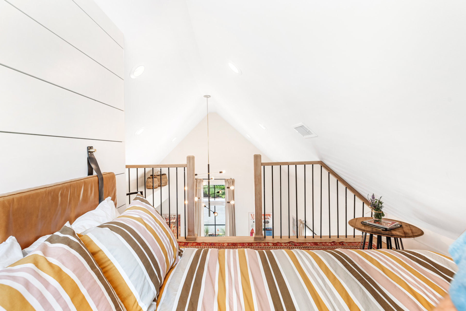 Loft bed in striped linen with tan leather headboard under the vaulted ceiling