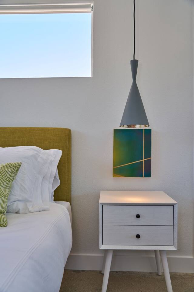 Bedroom with chartreuse linen headboard, grey pendant and abstract painting