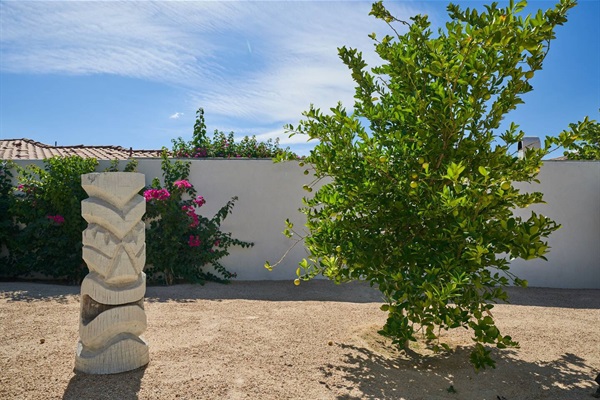 Carved stone totem and citrus tree against a white garden wall
