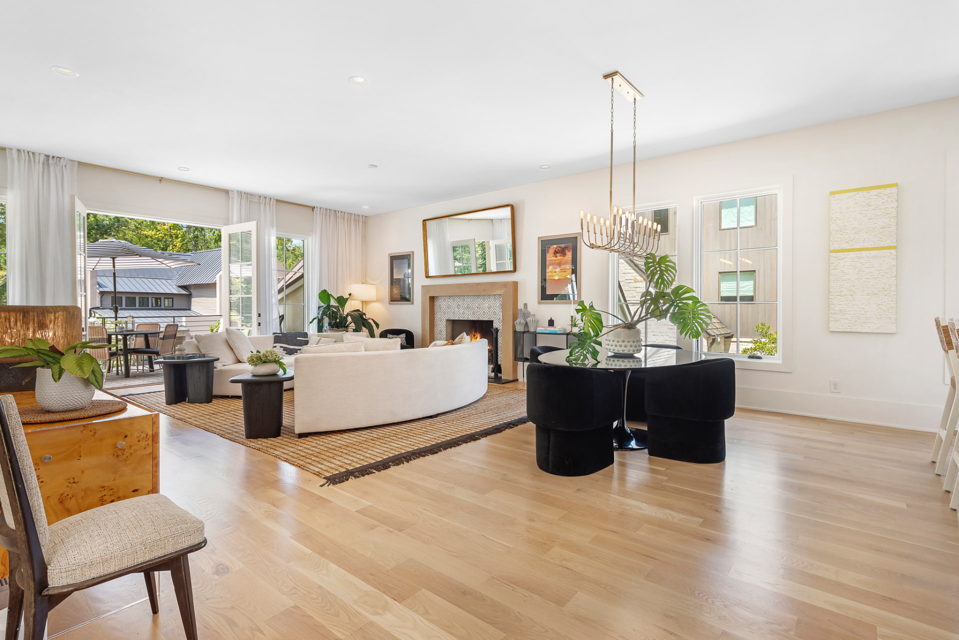 Open living and dining room with curved ivory sectional, stone fireplace and brass linear chandelier