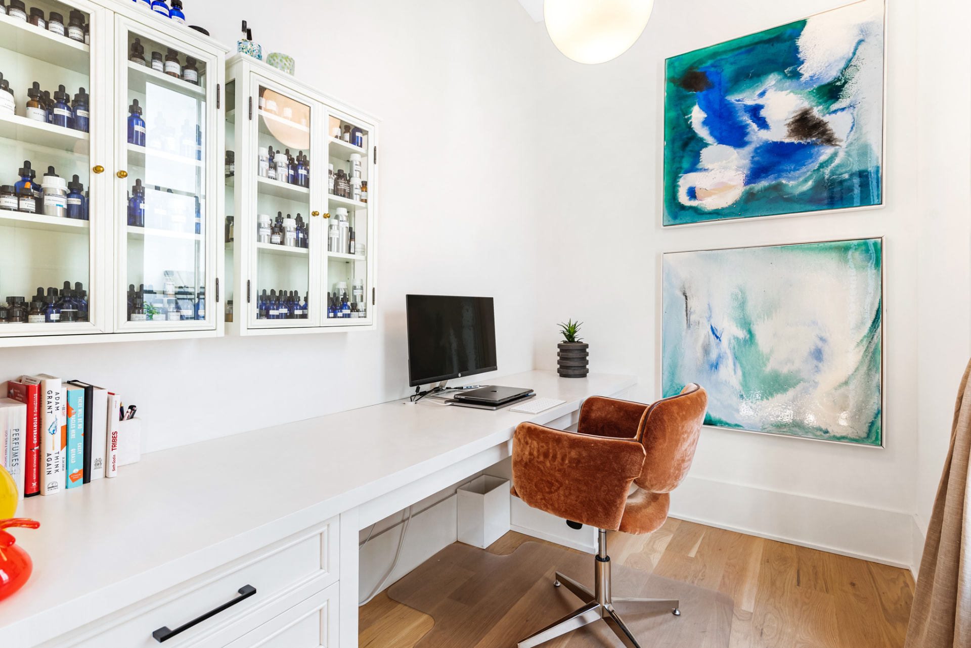 Built-in study desk with apothecary glass cabinets and blue-green abstract canvases